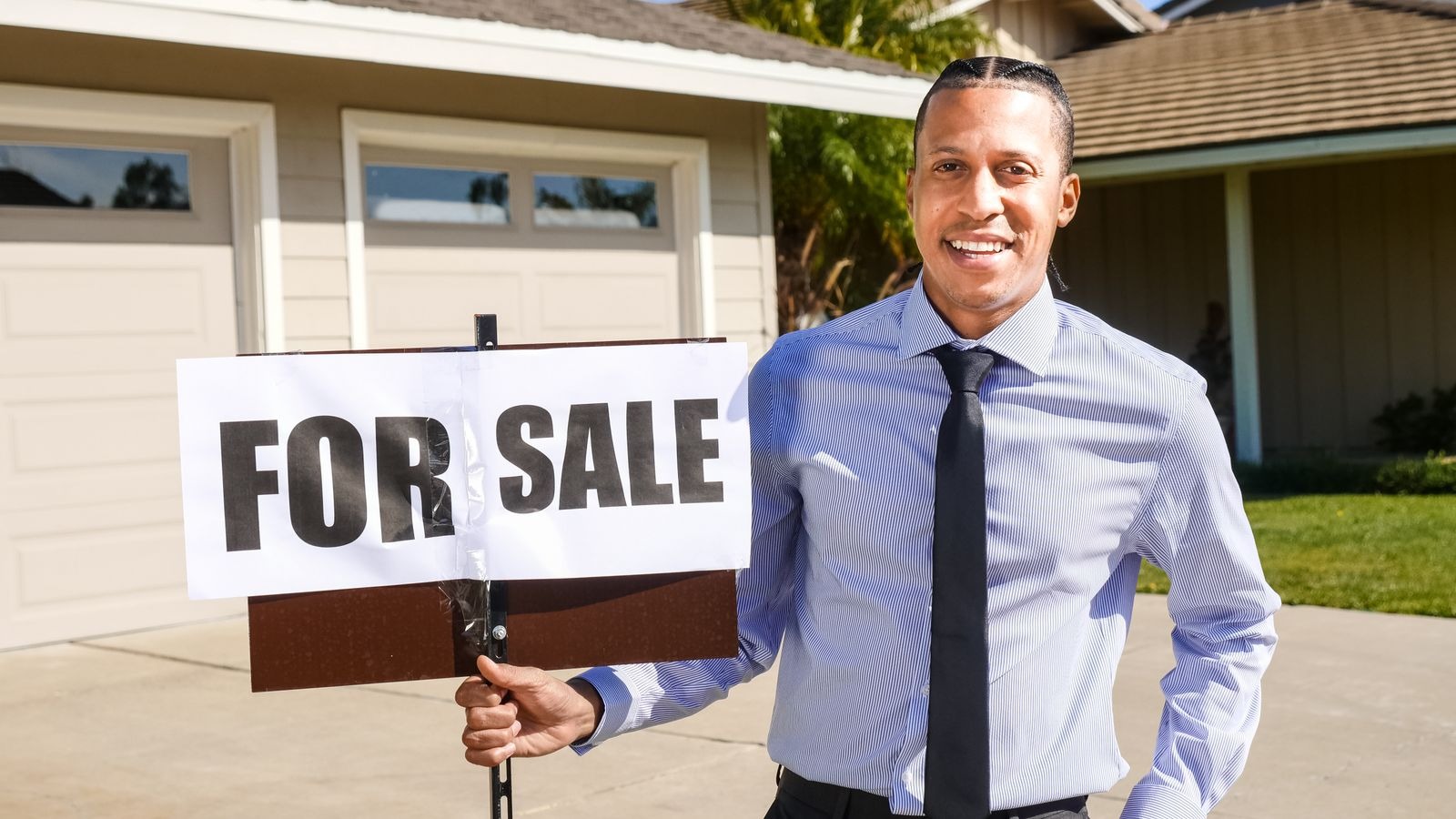 Agent immobilier tenant un panneau À vendre devant une maison